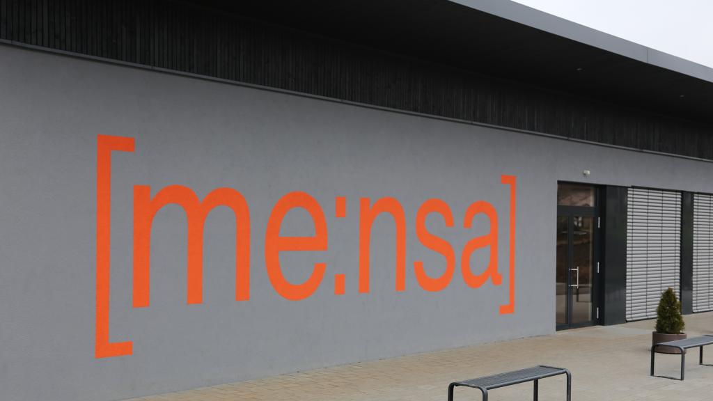 Oranger Schriftzug "Mensa" auf der Fassade der PAGS Schule in Kühlsheim
