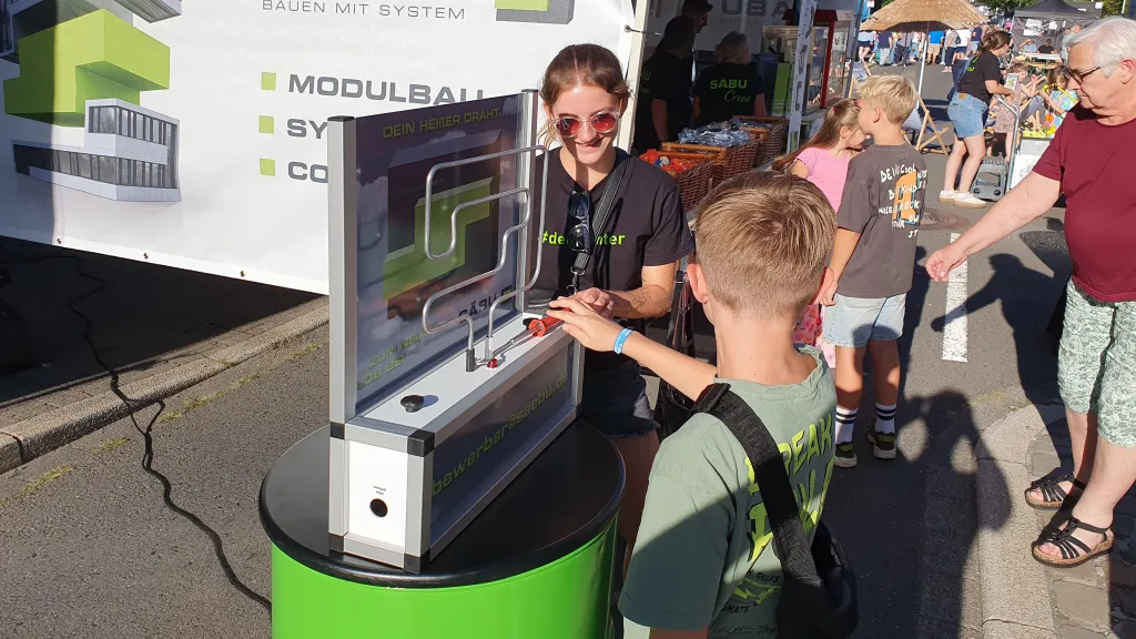 Ein Junge probiert das Spiel „Heißer Draht“ am SÄBU-Stand auf der Langen Nacht in Morsbach aus, während eine Betreuerin zuschaut.