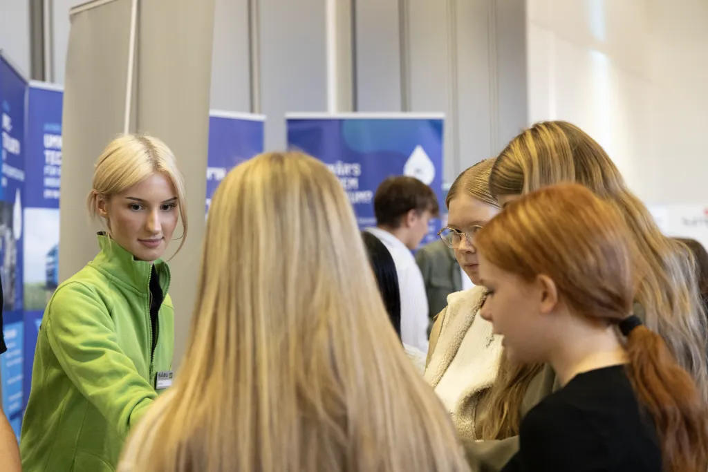 Azubine steht vor vier Schülerinnen und überreicht ihnen unsere Ausbildungsflyer auf der Ausbildungsmesse von der Leonardo da Vinci Schule in Morsbach.